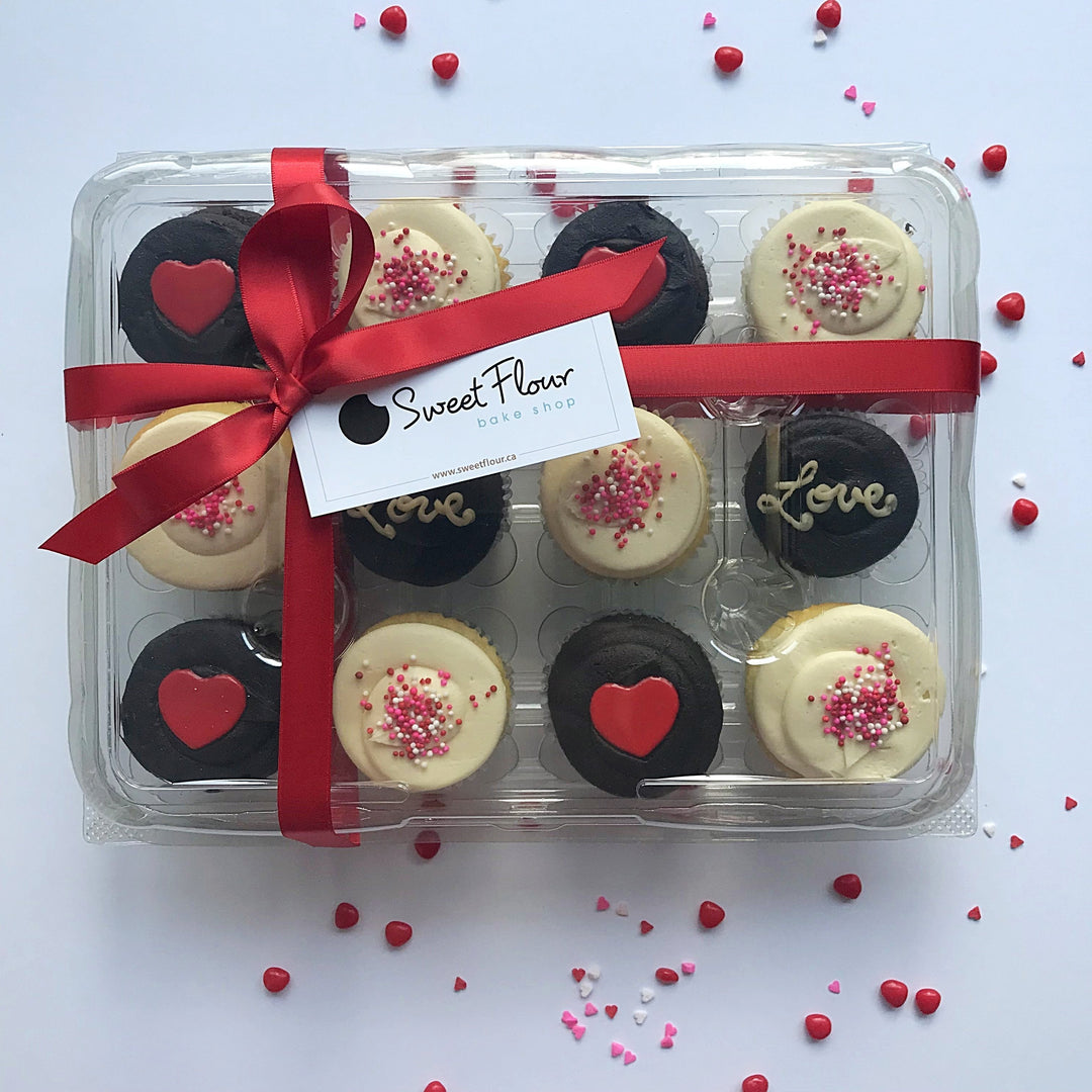 One dozen packaged Valentine's Day cupcakes with love and red hearts frosted on top with red ribbon