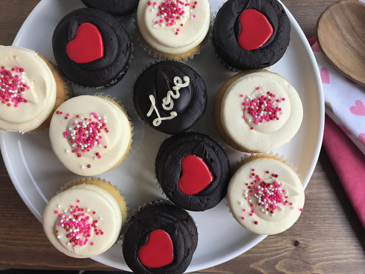 One dozen Valentines Day cupcakes with love and red hearts frosted on top on plate